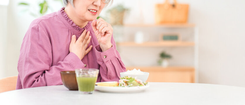 A gray-haired senior woman choking while eating (aspiration pneumonia, swallowing disorder)