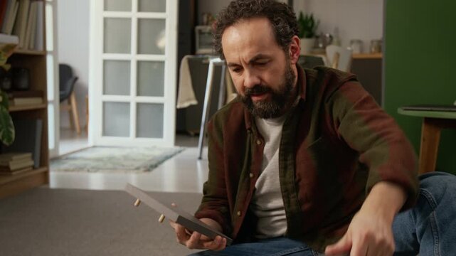 Medium tilt-up shot of angry 50-year-old Caucasian man fitting pieces of flatpack locker together, then swearing at mistake during assembly, checking manual and removing dowels with pliers