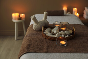 Herbal sacks, rocks and burning candles on massage bed in spa center, closeup