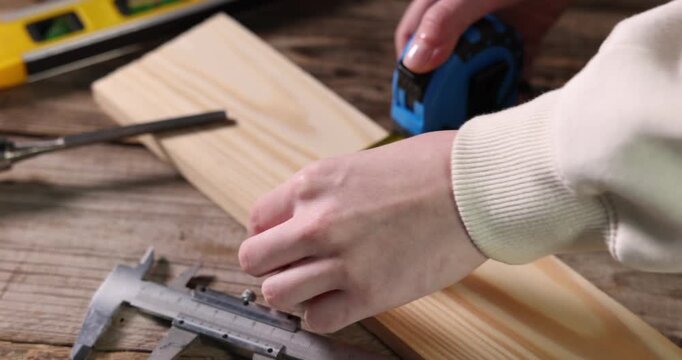 Woman measuring plank with tape at wooden table, closeup. Camera moving in