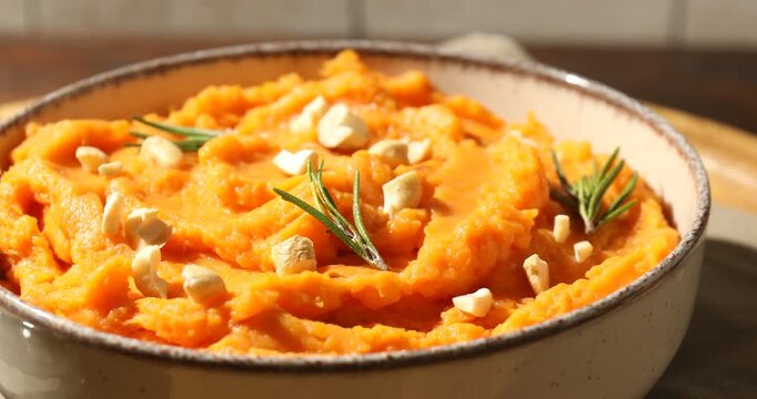 Delicious mashed sweet potato with cheese and rosemary in bowl on table, spinning. Closeup view