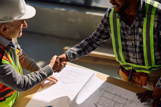 Close up of black worker handshaking with building contractor at construction site.
