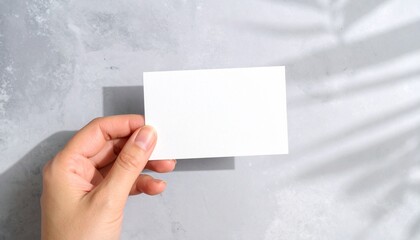 Obraz premium Hand holding a minimalist white card mockup on grey background.