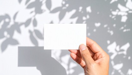Obraz premium Hand holding blank white business card mockup with bright sunlight leaf shadows