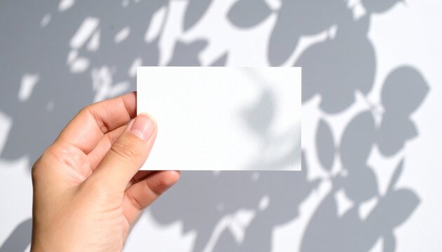 Hand holding blank white business card mockup with subtle leaf shadows