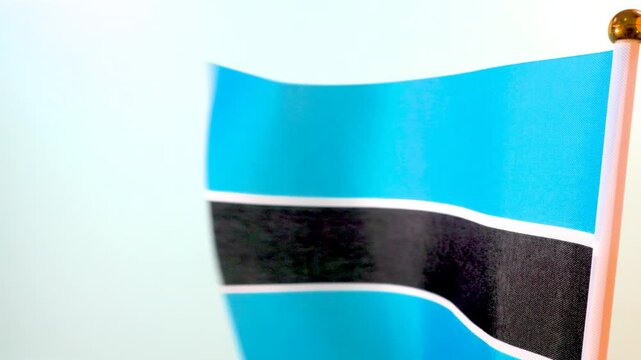 A detailed slow-motion shot of the Botswana flag waving. The sky-blue, black, and white stripes are prominently displayed, representing the nation's "Pula" (rain) and its commitment to unity.