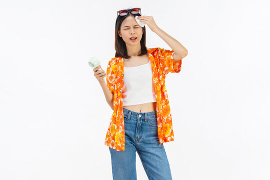 Young Asian woman in summer wearing floral shirt holding fan to cool herself with suffers from too hot weather in white background
