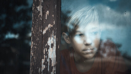 Thoughtful boy looking through old window reflecting sky, depression
