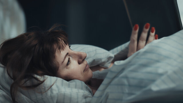 Woman in bed using smartphone with red nails in cozy bedroom, have fun and enjoy