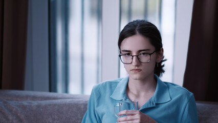 Young Woman Drinking water While Sitting on Couch Indoors, A serious girl came up with a plan for...