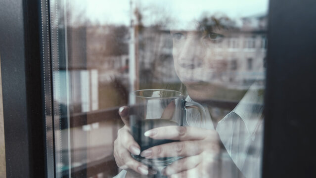 Woman Looking Through Window Holding Glass of Water, pensive woman