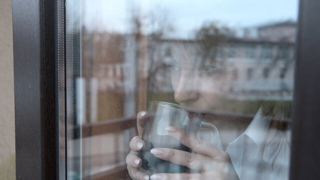 Pensive woman drinking coffee and looking through window reflect, a woman looks thoughtfully out the window