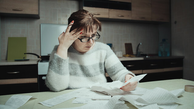 Stressed Woman Reviewing Bills and Receipts at Home Kitchen Table, The woman is surprised by the money spent