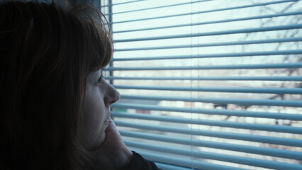 Fototapeta premium happy Woman Looking Outside Through Window Blinds in Thoughtful Mood in the evening