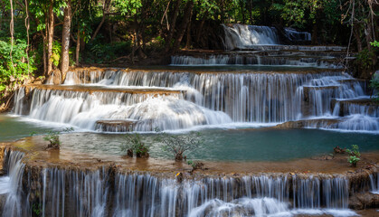 Tiered waterfall cascades through lush green forest. Sri Nakarin Dam National Park, Kanchanaburi, Thailand. Tropical jungle surrounds flowing stream. © Eugene Ga