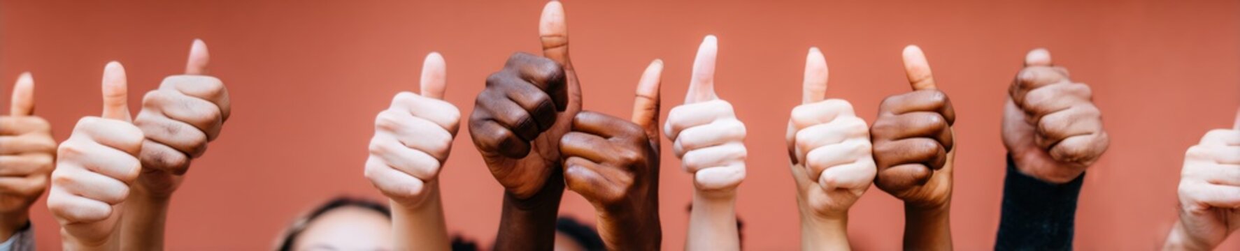 Many diverse hands giving thumbs up gesture together for collective success and achievement, multicultural group showing approval against a cherry red background wall