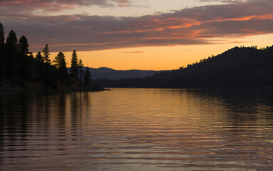 Fototapeta premium Serene lake at sunset with trees and mountains in the background