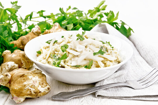 Salad of Jerusalem artichoke and eggs in plate on white wooden board