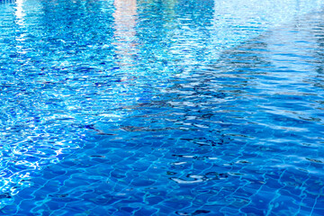 Clear blue swimming pool water with sunlight reflections and ripples. The tiled bottom is visible through the crystal clear surface. Perfect for summer, vacation, or resort background themes. © sirawut