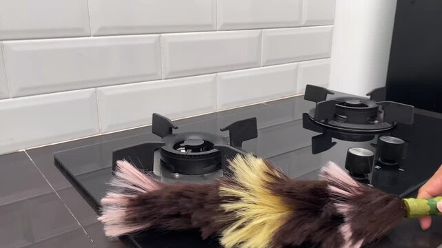 Cleaning a modern gas stove top with a feather duster