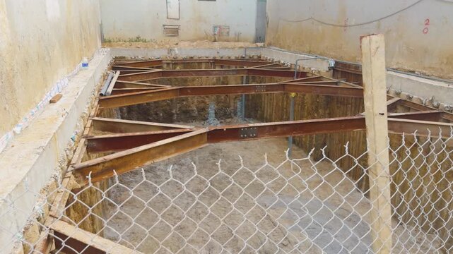 Construction site with a deep excavation supported by a temporary shoring system of steel beams, preparing the ground for laying the foundation of a new building project