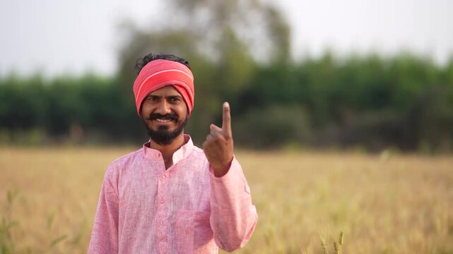 young indian farmer showing voting finger standing at field	