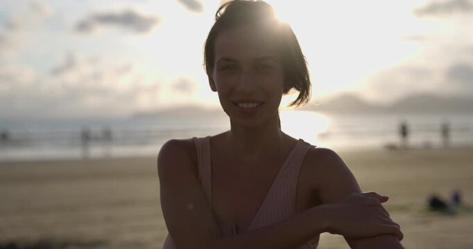 Attractive woman on beach at sunset catches eyeline and looks directly into camera smiling and laughing