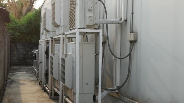 Row of outdoor air conditioner compressor units installed on wall in narrow alleyway with sunlight and lens flare