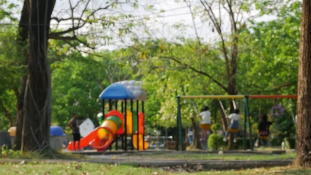 Blurred background of colorful children playground in public park with swings and slide at sunset