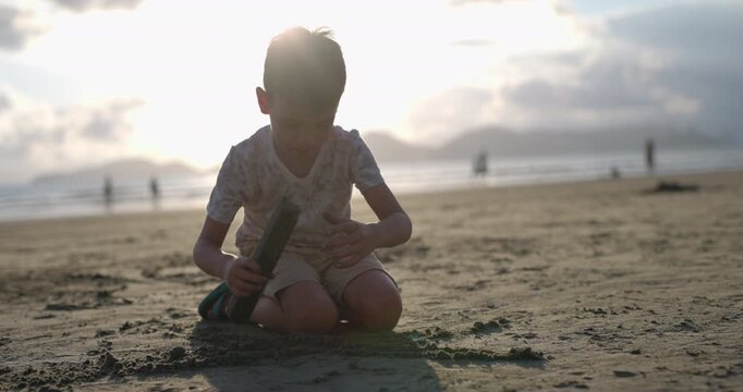 Young boy using sticks to dig in sand on beach