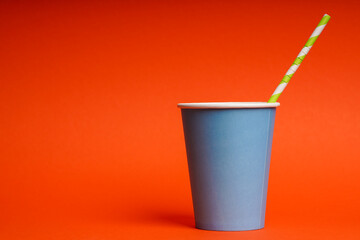 Blue paper cup with striped straw on orange background