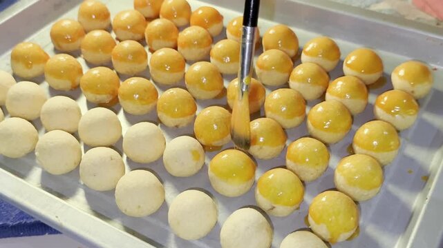 Close up process brushing egg glaze on traditional Indonesian nastar pineapple cookies arranged on tray during preparation for Eid celebration.