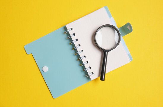 Notepad with a magnifying glass on a yellow background