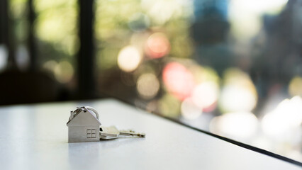 House keys with silver home keychain on table for real estate concept. New property ownership, mortgage loan, housing investment and residential moving service in bright bokeh background.
