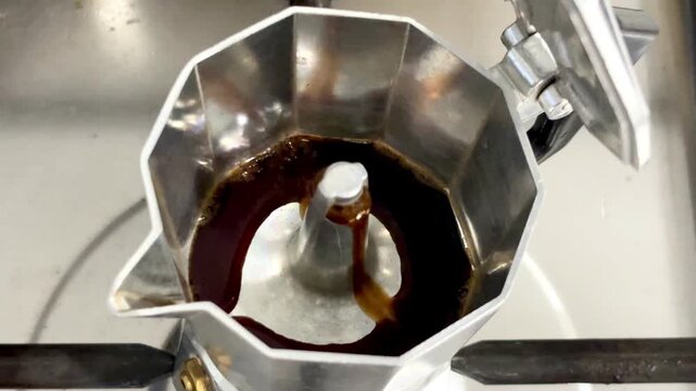 Close up of coffee brewing from a moka pot on a kitchen stove. Fresh coffee flowing from the center spout during the brewing process.