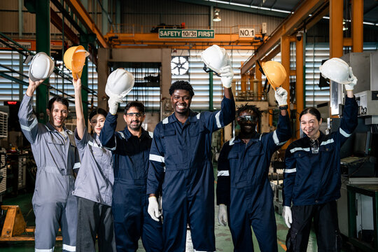 Factory workers raising safety helmets celebrating teamwork success in manufacturing plant, industrial workers motivation and positive factory workplace culture