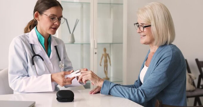 Female doctor placing fingertip pulse oximeter onto woman patient finger, to measure blood oxygen saturation, checking heart rate during medical consultation in clinic office. Health care services