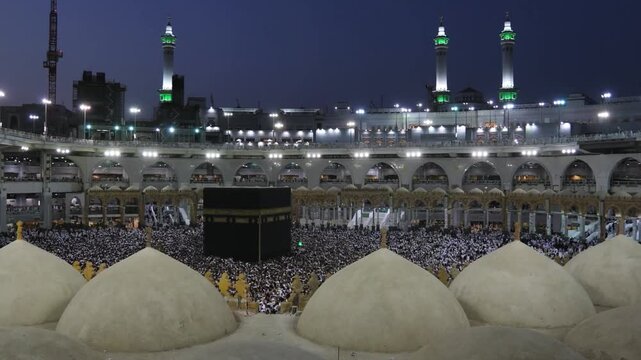 Scenic view of Holy Kaaba at night with illuminated minarets and pilgrims in Mecca. Aetekaaf time during Ramadhan .