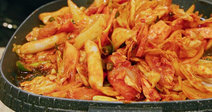 The process of cooking Korean-style spicy stir-fried spring chicken on an iron plate involves stir-frying tender chicken meat, chewy rice cakes, and kimchi in a bright red spicy sauce, releasing an en
