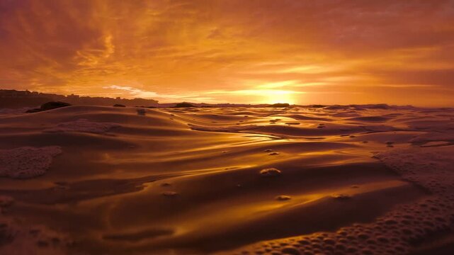 Slow motion video of the rippling ocean surface at sunrise, filmed at water level as the burning red sky reflects across the sea at Bronte Beach, Sydney, Australia.