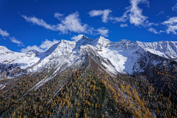 Fototapeta premium Drone view landscape of Shuangqiao Valley (Shuangqiaogou or Double Bridge Valley) in Mount Siguniang in Sichuan, China. Beautiful snow capped mountains with colorful autumn forest in sunny day.