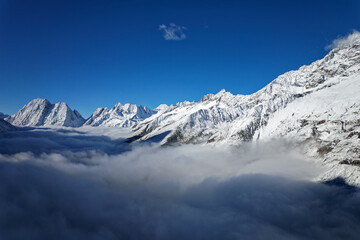 Obraz premium Drone view landscape of Shuangqiao Valley (Shuangqiaogou or Double Bridge Valley) in Mount Siguniang in Sichuan, China. Beautiful snow capped mountains over white clouds in sunny day.