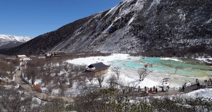 Beautiful view of colorful calcite pools of Five colors pond in Huanglong valley, scenic and historic interest area in Sichuan, China. Tourists walking on boardwalk, panoramic shot on sunny winter day
