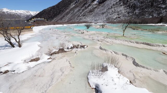 Famous travertine terraces and colorful pools in Huanglong National Park, Sichuan, China, world heritage site covered in snow. Panoramic shot of five colors pond area. Sunny winter day in mountains