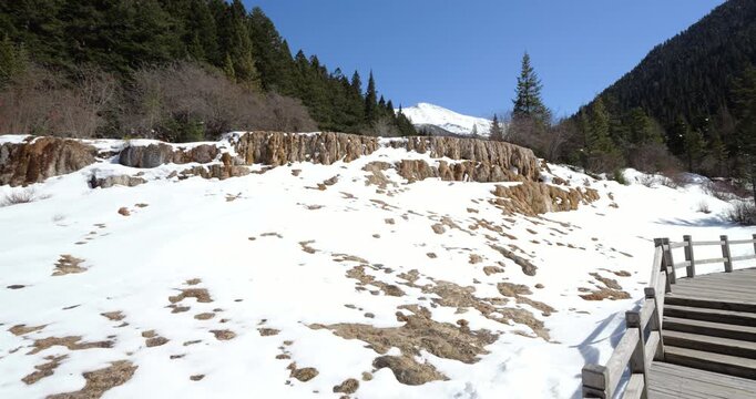 Point of view, looking to snow covered travertine terraces in the Huanglong valley at late march. Camera move forward to dry waterfall-like place. Mountains and blue sky on background