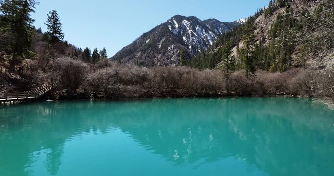 Stunning natural landscape of vibrant turquoise lake with and mountains with slight amount of snow on slopes at background. Rare view of popular Jiuzhaigou Valley without people visible