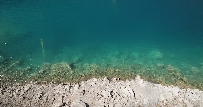 High angle view from elevated platform to shore of mountain lake with stunning clear turquoise water, details of Jiuzhaigou National Park, world heritage site famous for its colorful ponds and lakes.