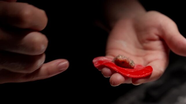 Closeup of hands shaping bright red dough wrapper around seasoned meat filling, carefully folding delicate dumpling skin in low light kitchen setting