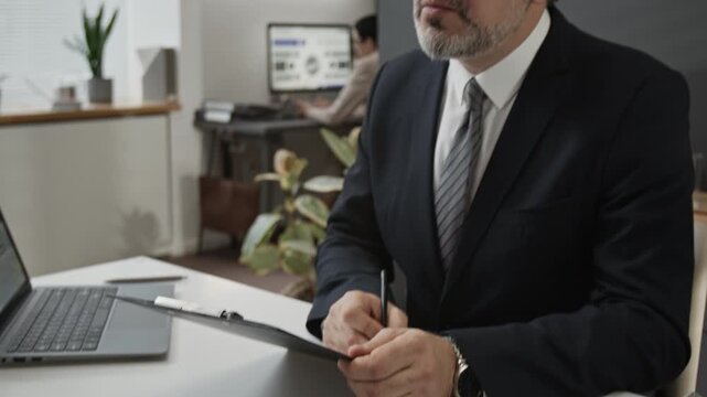 Gen Z male candidate answering questions of formally dressed mature hiring manager who looking through mans application form during job interview