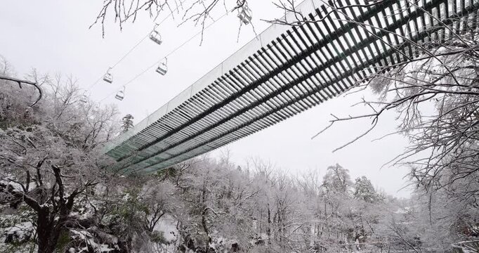 Low-angle shot of closed wooden plank bridge encased in thick glaze ice at Tianmen Mountain. Shimmering icicles and frozen surfaces create glass-like appearance after rare March weather anomaly
